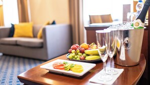 Une chambre d’hôtel avec une table à manger dressée, agrémentée de fruits, d’une bouteille de champagne et d’un verre à vin.