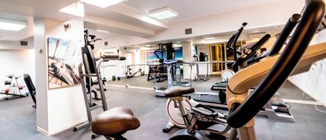 A gym with various exercise equipment, including treadmills and stationary bikes, and a mirrored wall.
