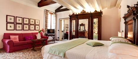 A hotel room with a large bed, a red sofa, a television, and a wooden cabinet.