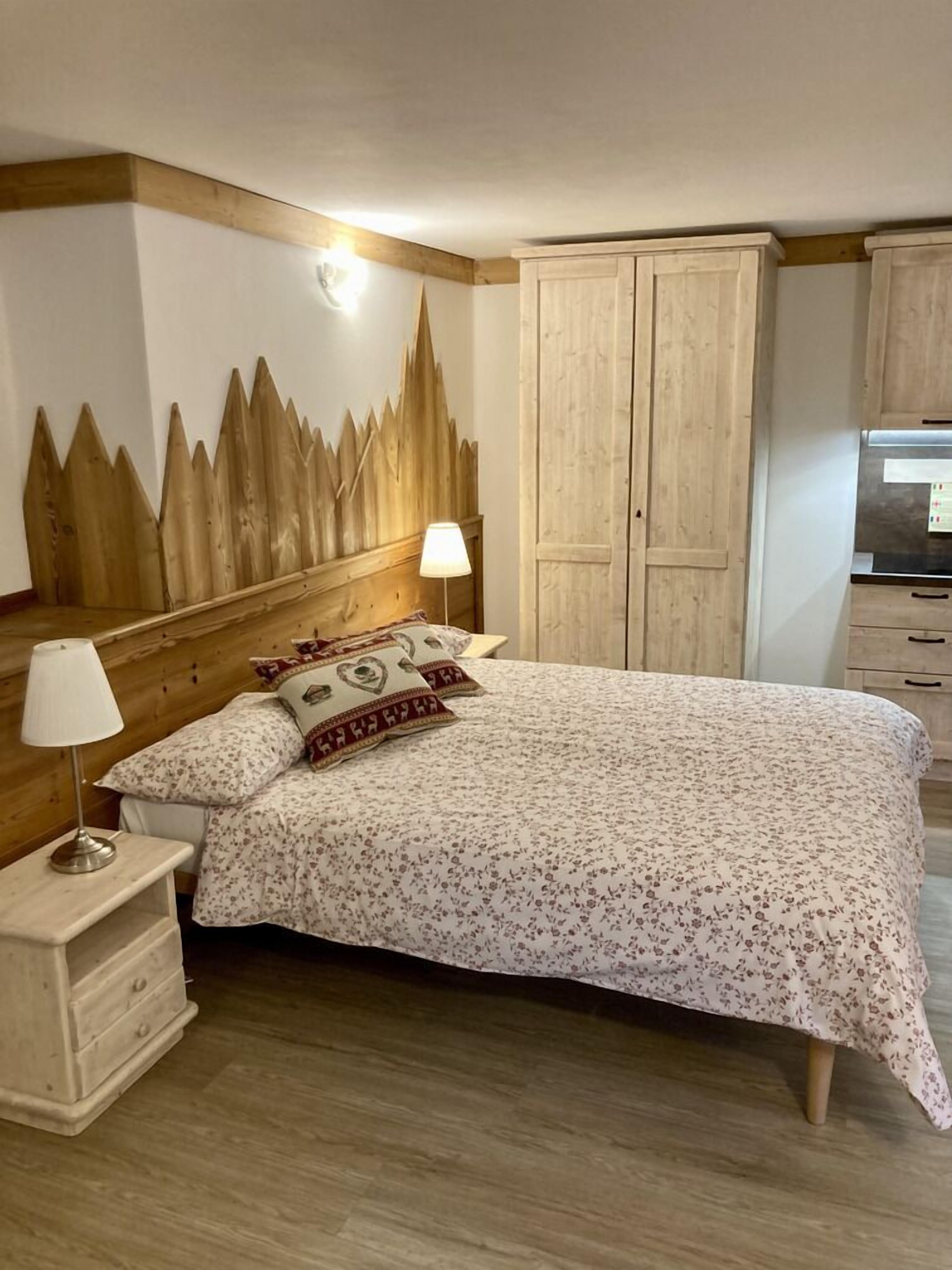 Een slaapkamer met een houten hoofdbord, een bed met bloemenbeddels, een nachtkastje met een lamp en een kledingkast.