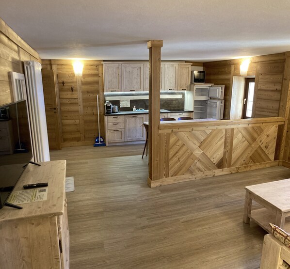 A rustic wooden interior with a kitchen area, wooden flooring, and a dining table.