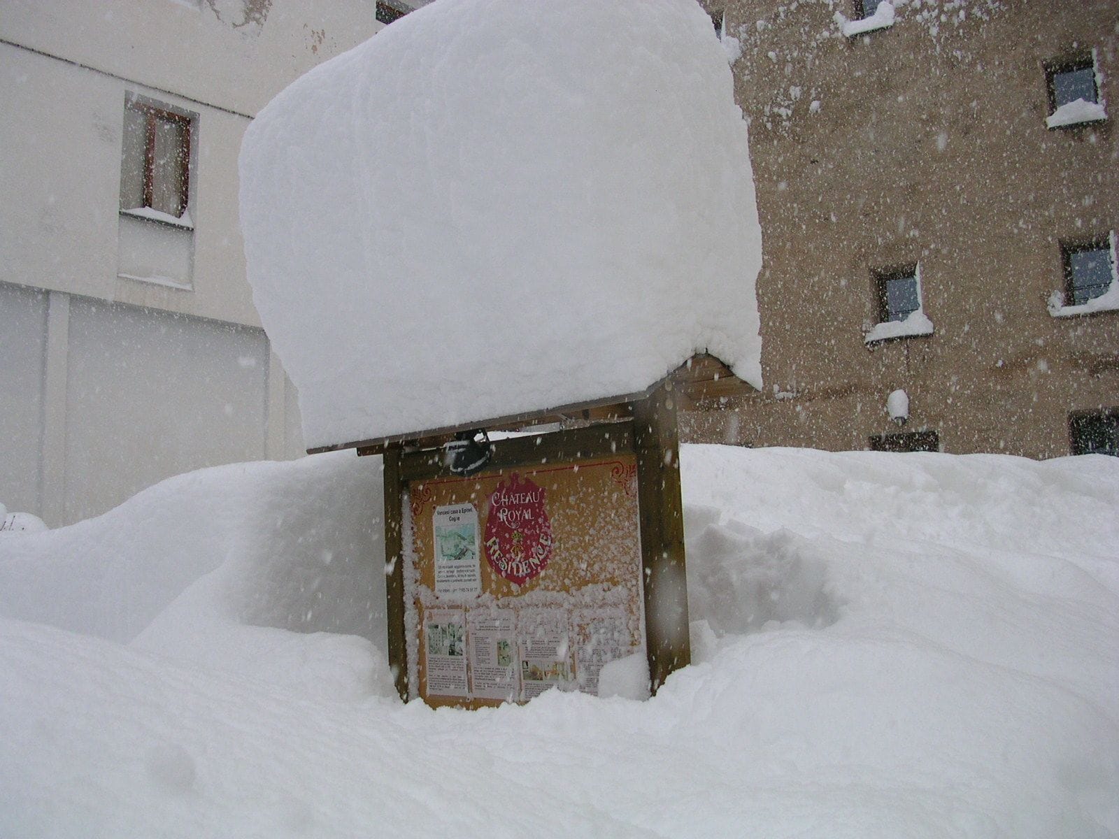 Un panneau d’affichage recouvert de neige, orné d’un emblème rouge, partiellement masqué par une forte chute de neige.