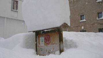 Un panneau d’affichage recouvert de neige, orné d’un emblème rouge, partiellement masqué par une forte chute de neige.