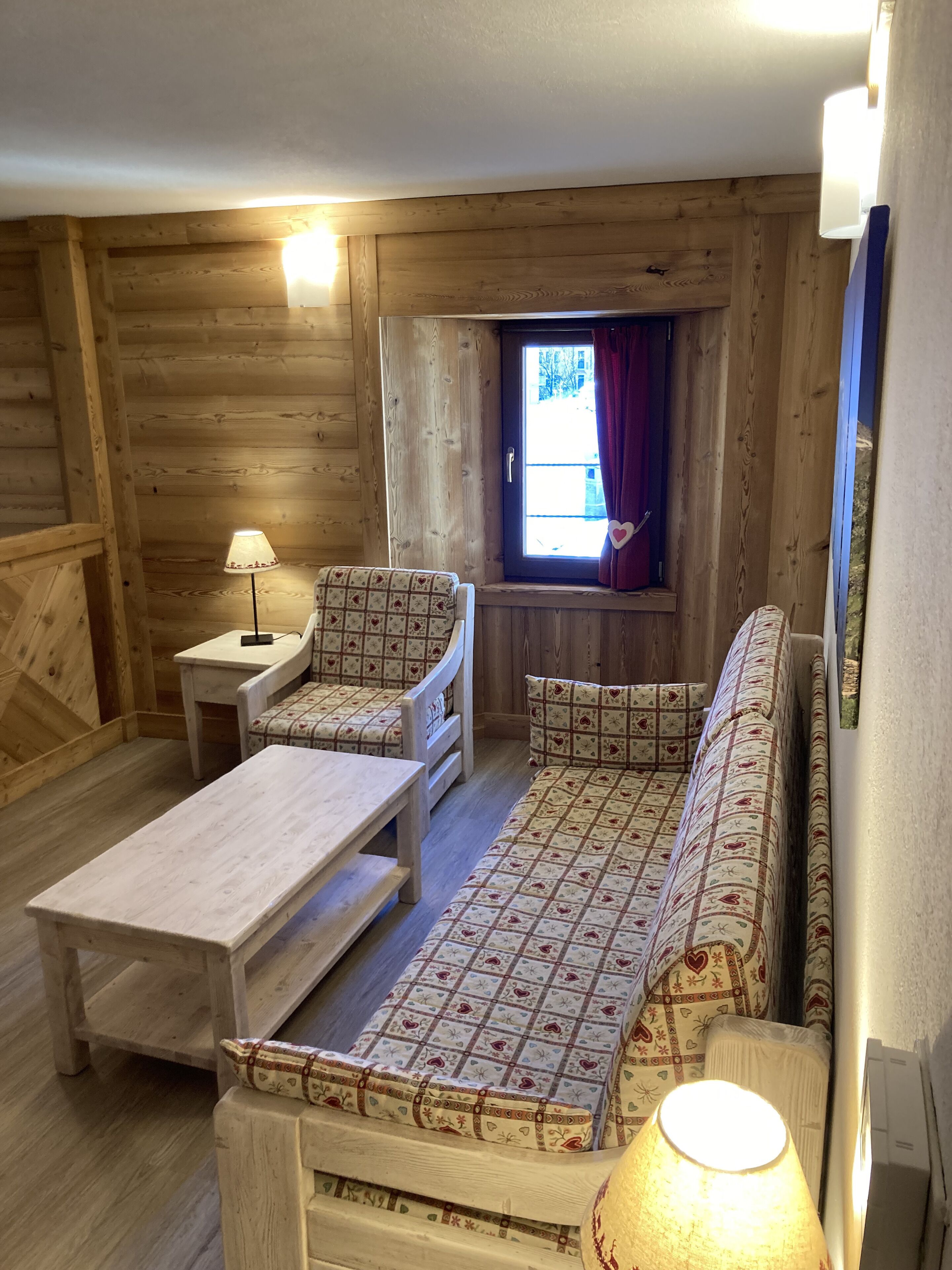 Un accogliente interno di una baita di legno con un divano, un tavolino e una lampada.