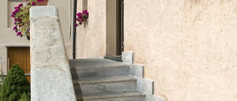 Una escalera de piedra conduce a la entrada de un edificio, con jardineras en la pared y una barandilla metálica.