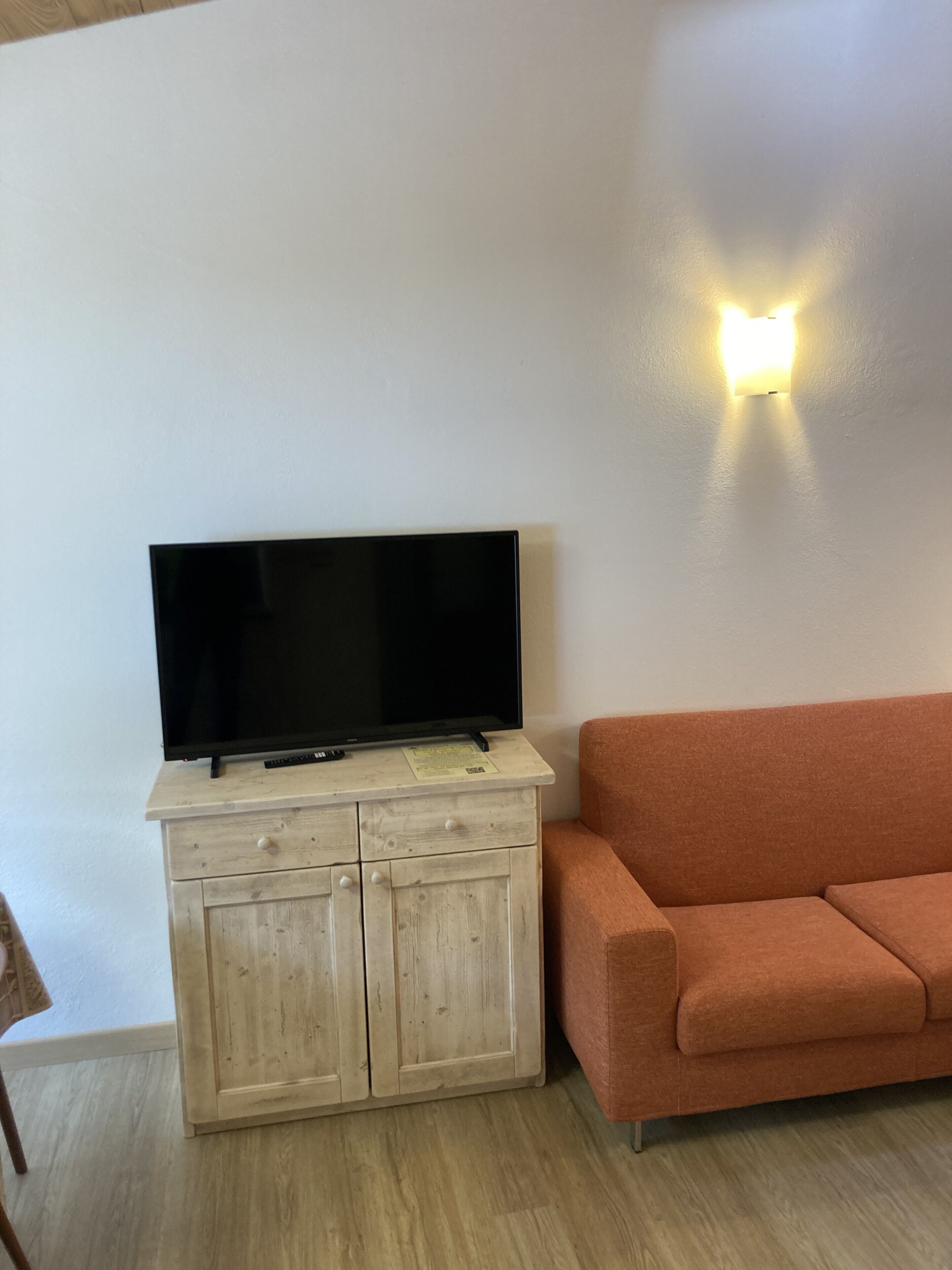 Een woonkamer met een televisie op een houten kast, een oranje bank en een wandlamp.