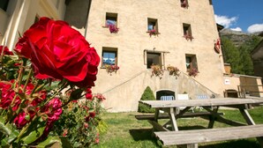 Un edificio con varias ventanas, algunas con jardineras, una mesa de picnic y un área verde al frente.