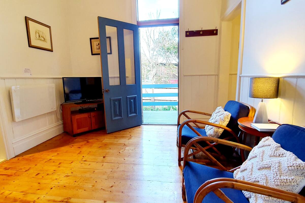 A room with a wooden floor, a blue sofa, a TV, and a door leading outside.