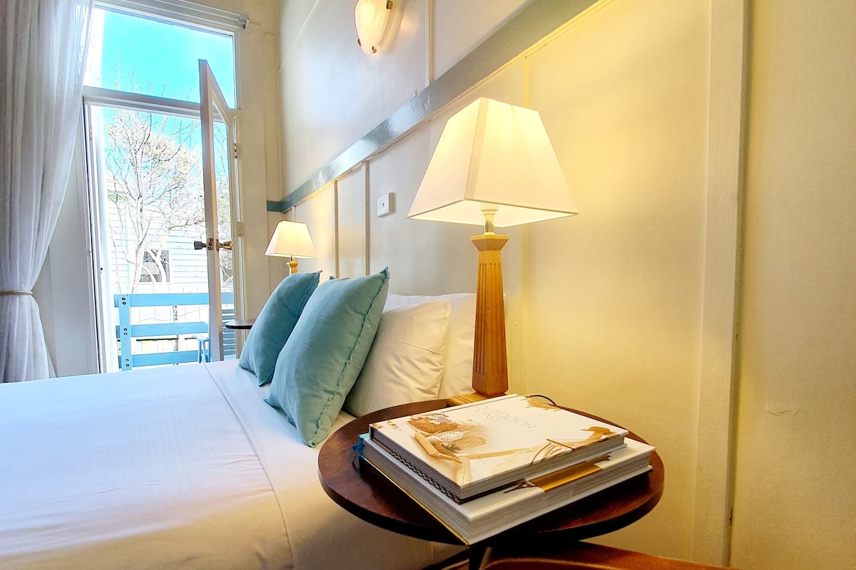 A hotel room with a bed, two pillows, a bedside table with a lamp, and a window with curtains.