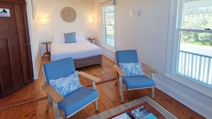 A bedroom with a bed, two chairs, a ceiling fan, a window, and a nightstand. - Point Lonsdale Guest House (Point Lonsdale)