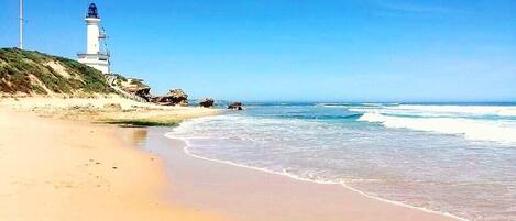 A beach with a lighthouse, sandy shore, and ocean waves.