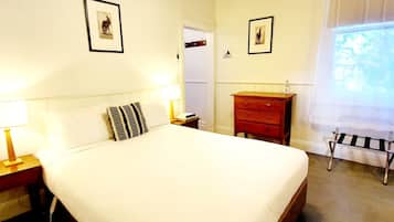 A neatly made bed with white bedding, a wooden nightstand with a lamp, a red dresser, and two framed pictures on the wall.