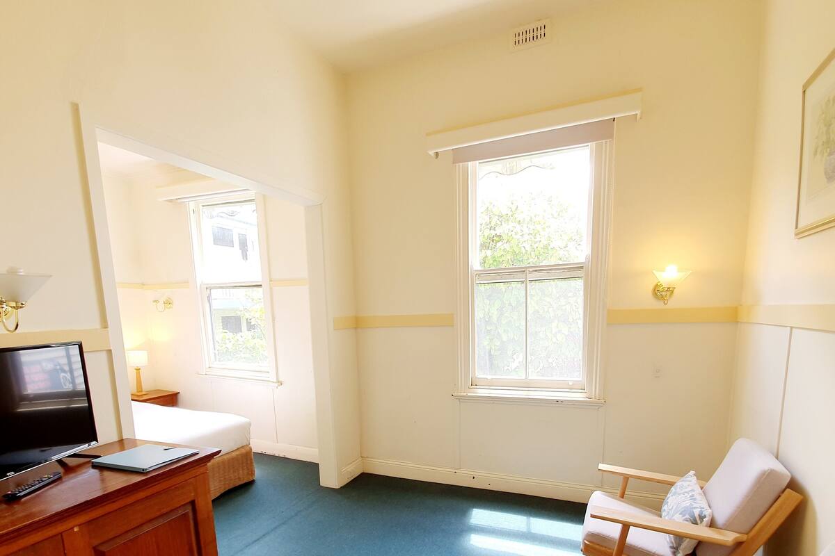 A hotel room with a bed, a desk with a TV, a chair, and two windows.
