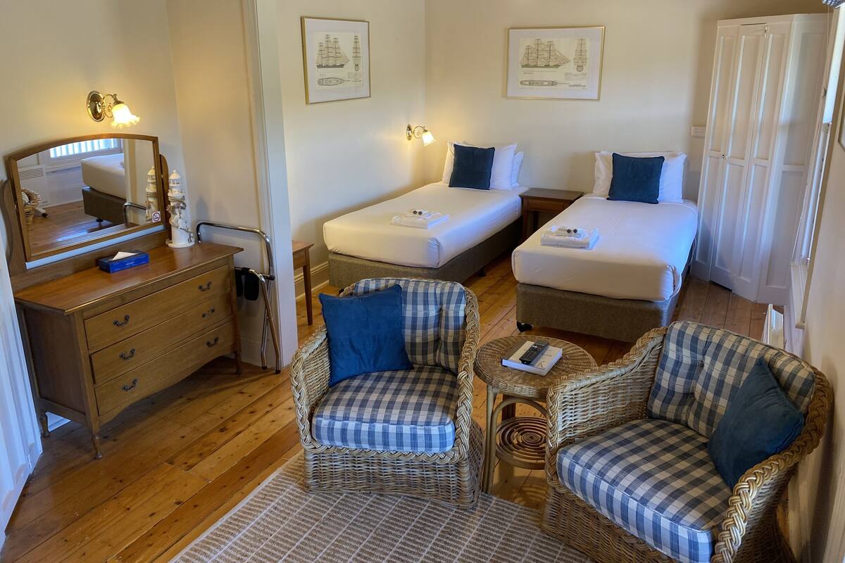 A hotel room with two beds, a dresser, a mirror, and two wicker chairs.