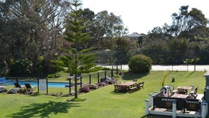 A pool area with lounge chairs and a table, surrounded by a fence and greenery. - Point Lonsdale Guest House (Point Lonsdale)