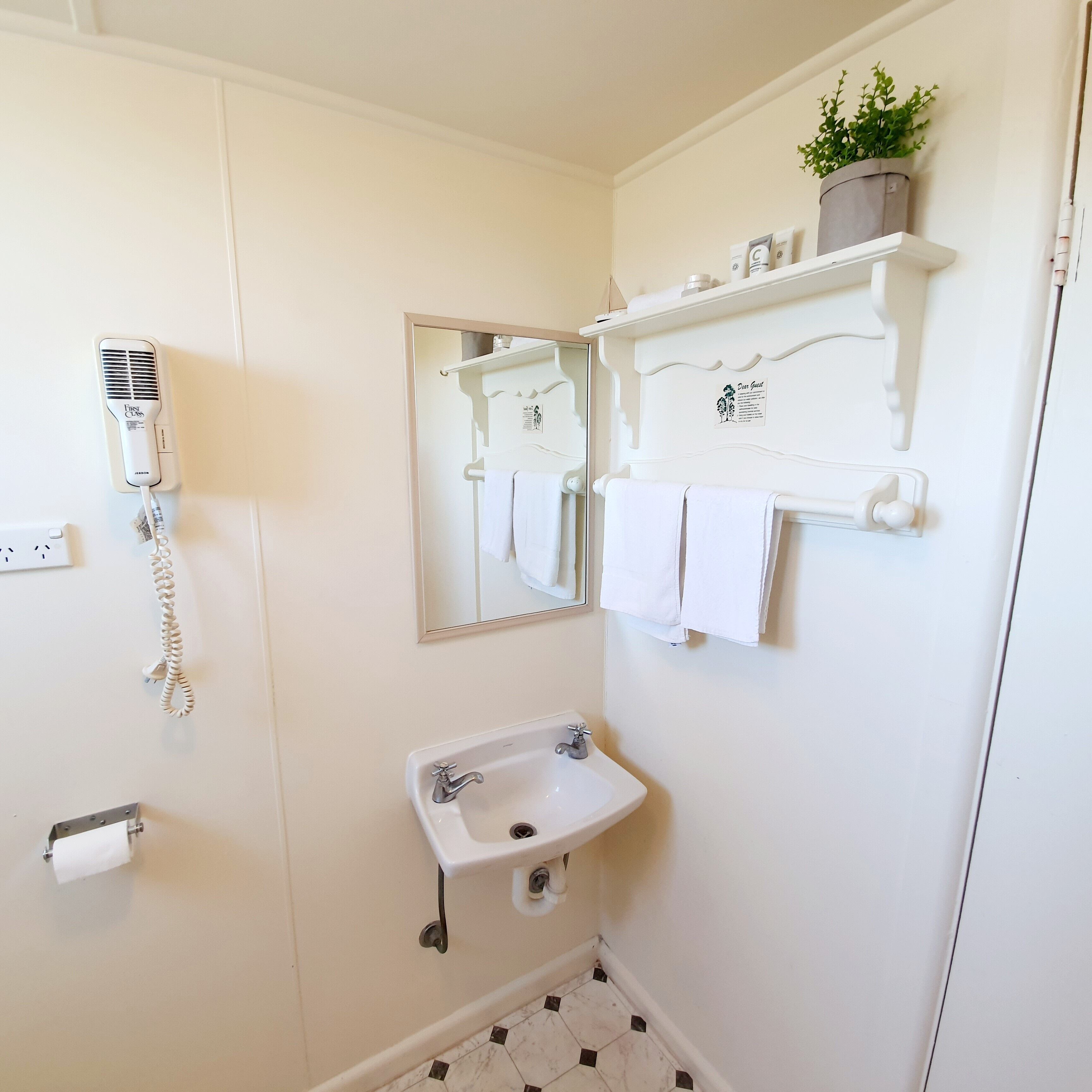 A bathroom with a hairdryer, a sink, a mirror, and a shelf with toiletries.