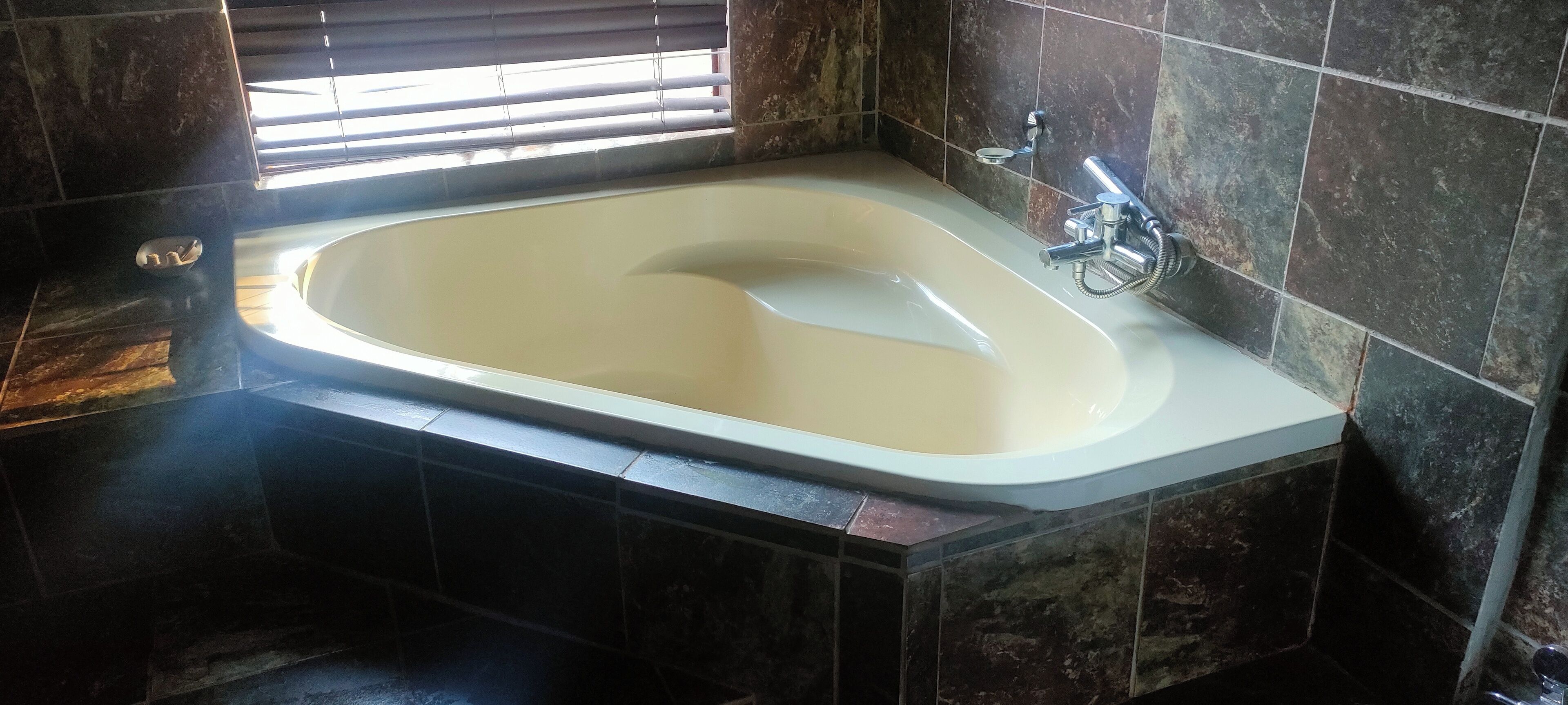 Une salle de bain avec une baignoire sur pieds, un espace douche et une fenêtre équipée de stores.