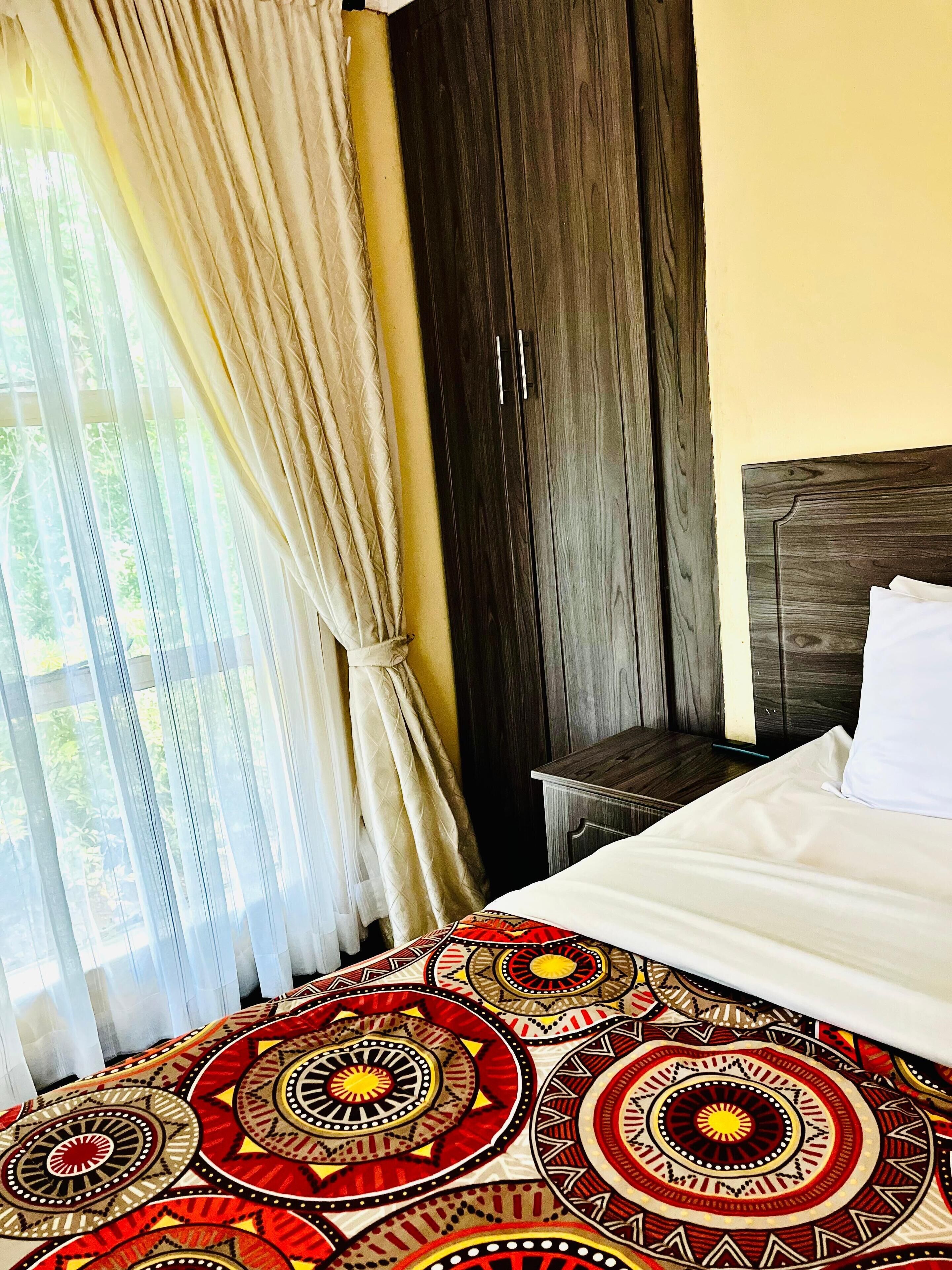 Quarto com cama, guarda-roupa de madeira e janela com cortinas.