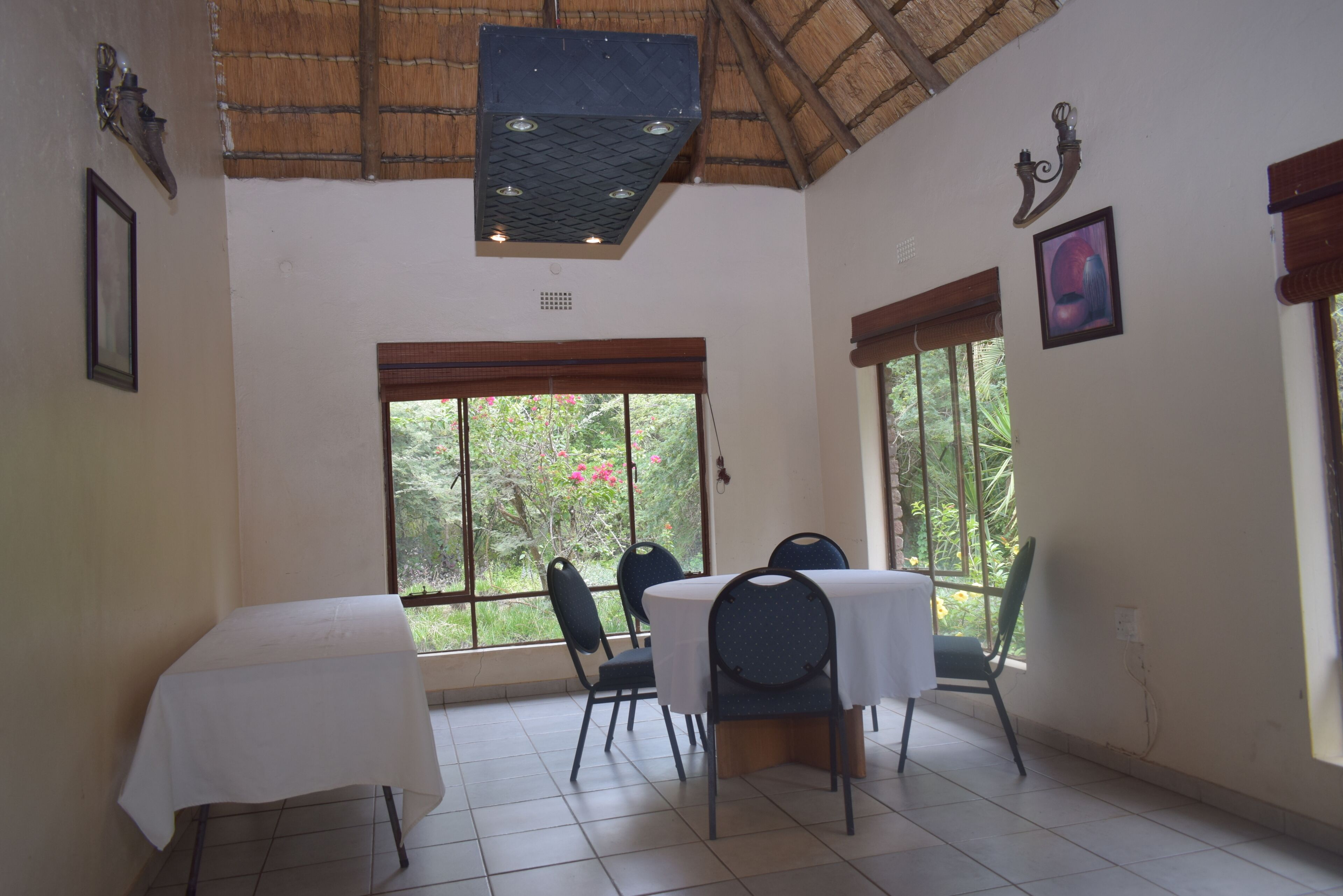 A dining area with a table and chairs, large windows, and a thatched ceiling.