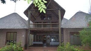 A rustic building with a thatched roof, a wooden balcony, and a gravel pathway leading to the entrance. - Copacopa Lodge and Conference Centre (Thulamela)