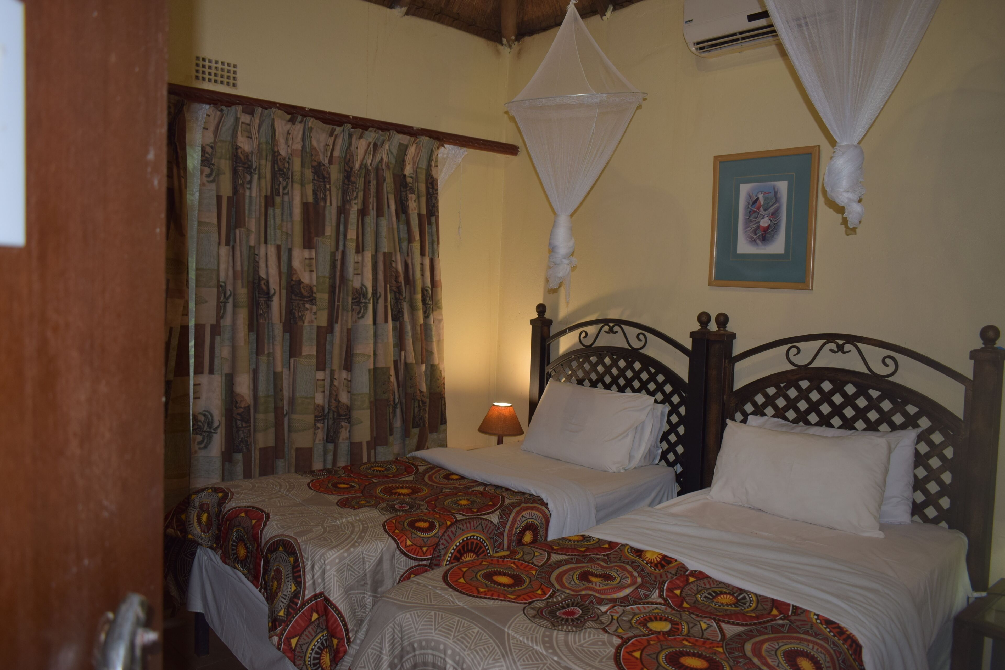 A room with two beds, a mosquito net, a framed picture on the wall, and a lamp.