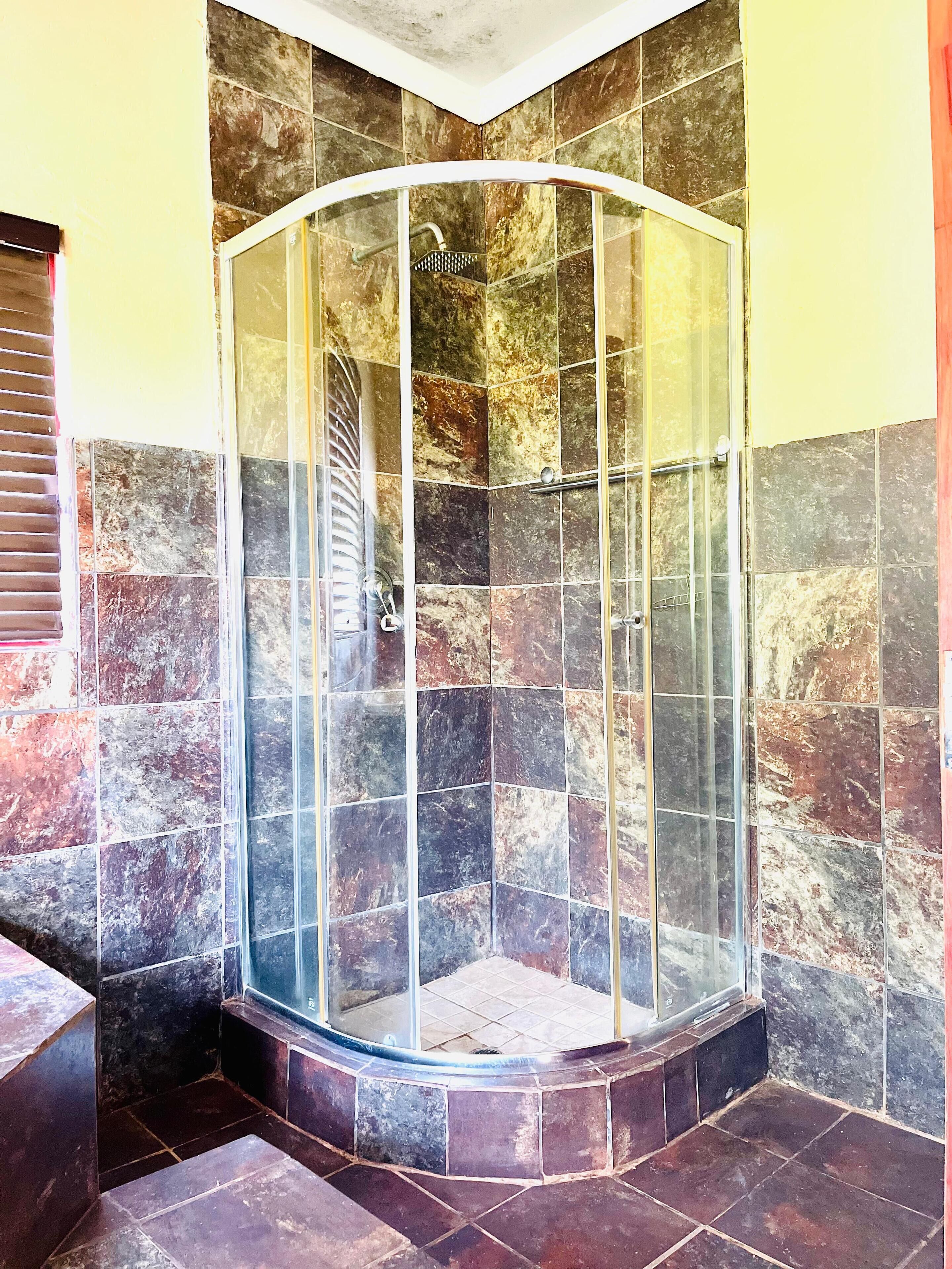 A corner shower with a glass enclosure, tiled walls, and a tiled floor.