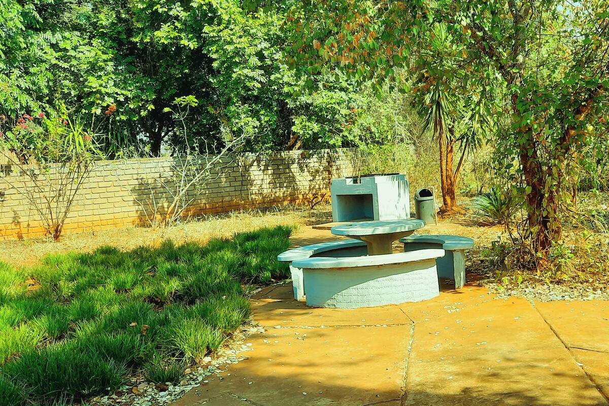 Un espace extérieur aménagé avec des éléments en béton, comprenant une table et des bancs, le tout entouré de verdure et d’arbres.