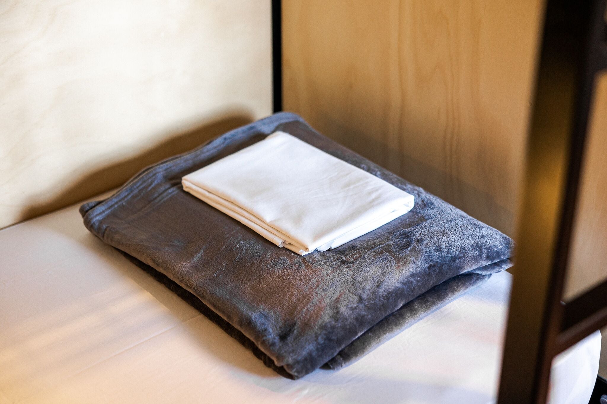 A neatly folded white towel on a dark gray pillow in a room with wooden furniture.