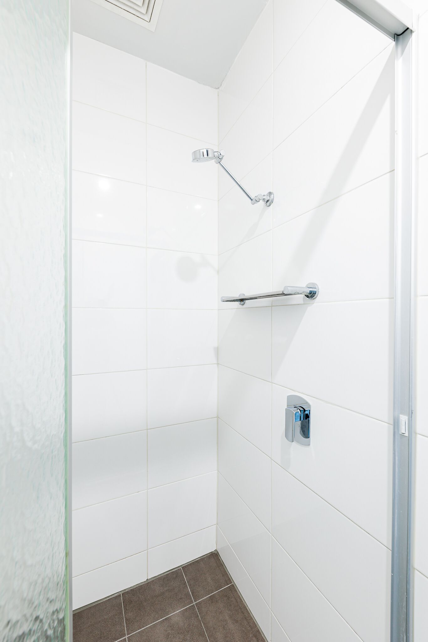 Ducha moderna con azulejos blancos, cabezal de ducha de mano y un perchero para toallas.
