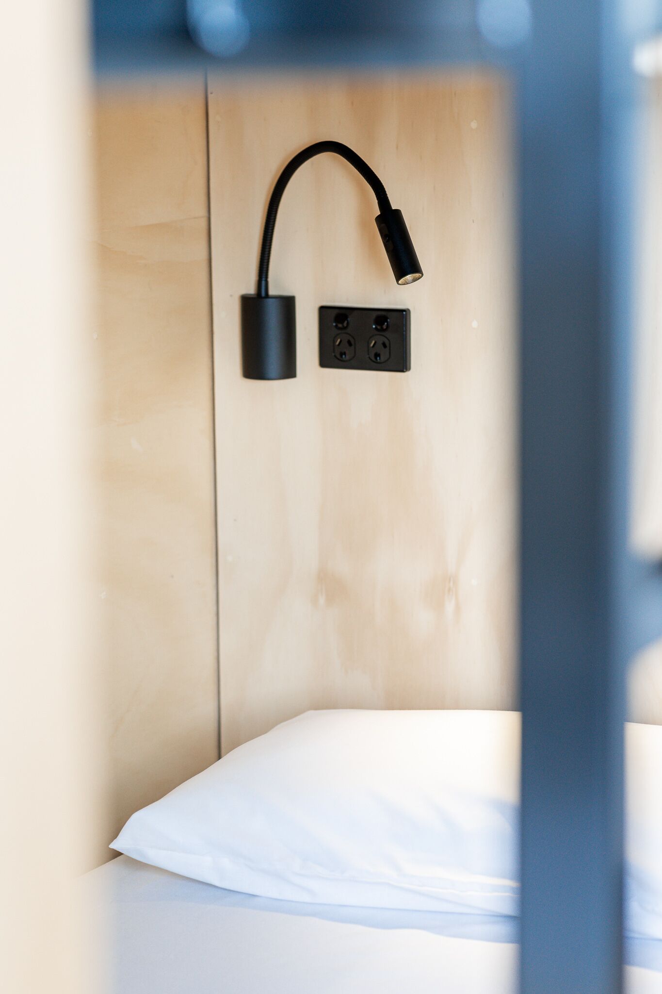 A bed with a white pillow and a black wall-mounted lamp.