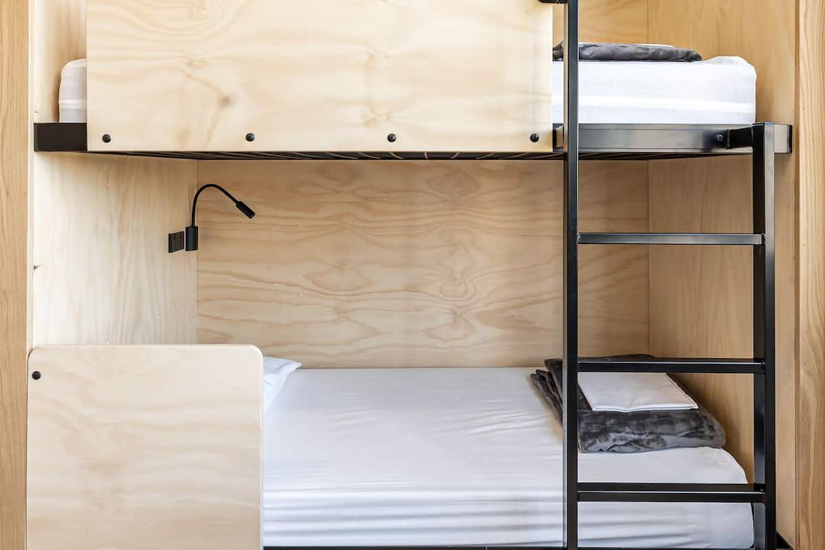 Una cama litera con estructura de madera y escalera metálica.