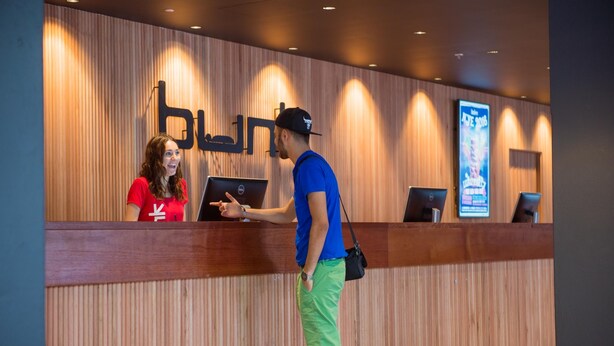 A reception desk with a wooden backdrop and a sign with Arabic script. - Bunk Backpackers (Fortitude Valley)