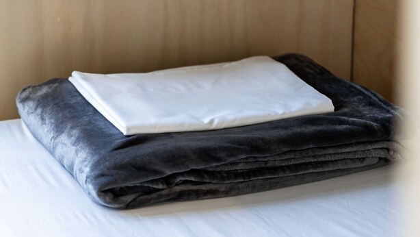 A neatly made bed with a white sheet and a folded blanket.