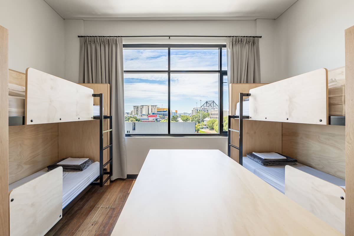 Una habitación con literas, un ventanal con vista a la ciudad y una mesa central.
