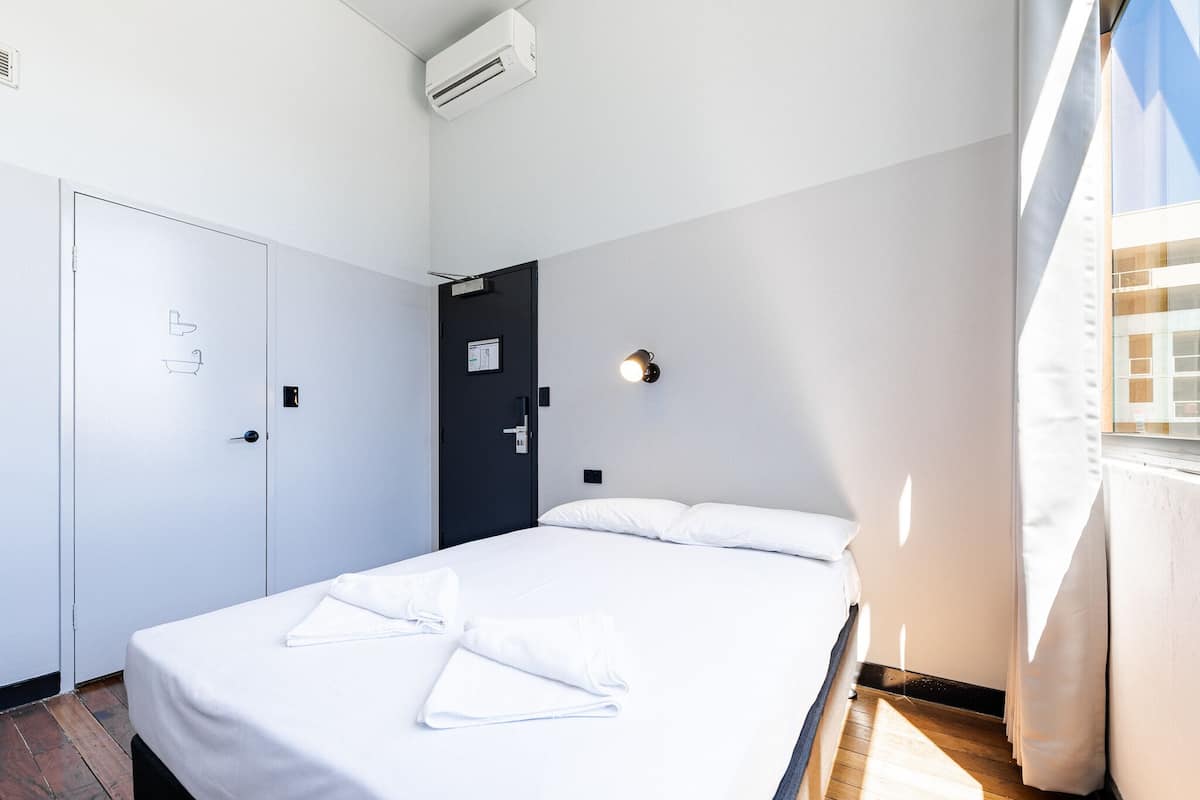 Una habitación de hotel con cama, armario, puerta y una lámpara fijada a la pared.