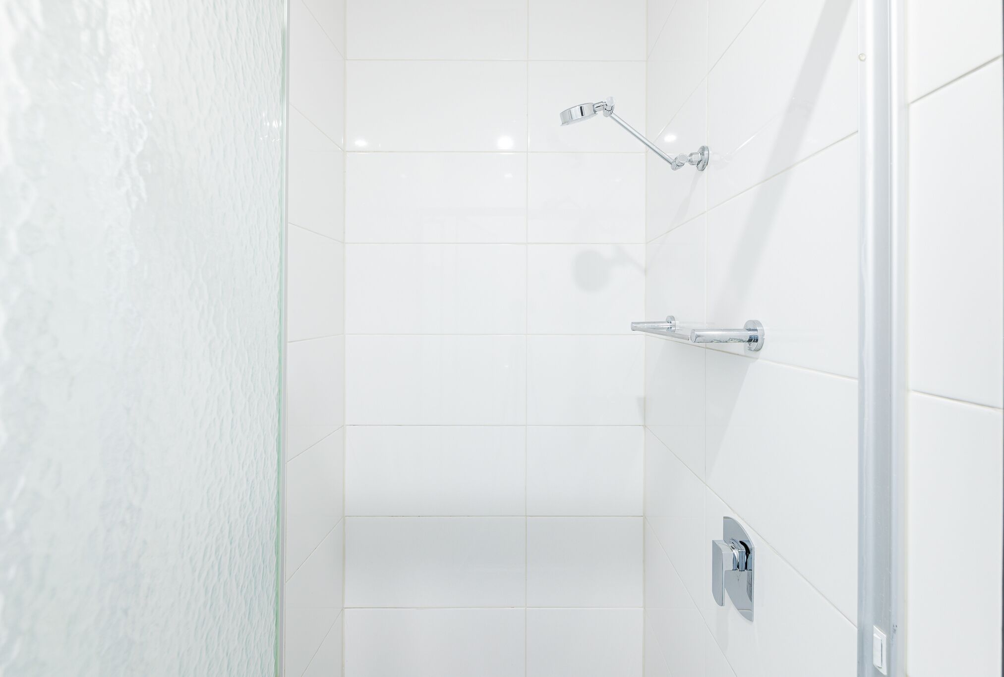 Ein Badezimmer mit weißen Fliesen, einer Duschbrause und einem Wasserhahn.