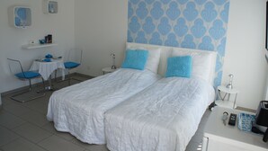 A hotel room with two beds, a small table, chairs, and a wall with a blue pattern. - Hotel Coco Aps (Esbjerg)