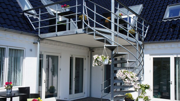 A modern outdoor area with a spiral staircase, potted plants, and outdoor furniture. - Hotel Coco Aps (Esbjerg)