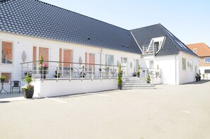 A white building with a grey roof, a balcony with metal railings, and potted plants. - Hotel Coco Aps (Esbjerg)