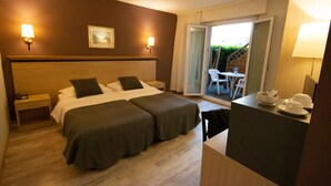 Une chambre d’hôtel avec deux lits, un bureau et une chaise. Il y a une fenêtre donnant sur un paysage verdoyant.