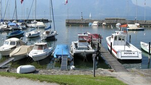 Un port de plaisance où sont amarrés différents types de bateaux, une jetée et, en arrière-plan, un paysage montagneux.