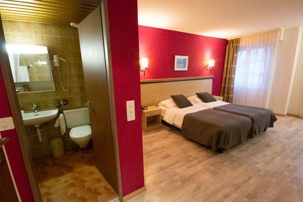 A hotel room with a bed, bedside table, and a bathroom with a sink and toilet.