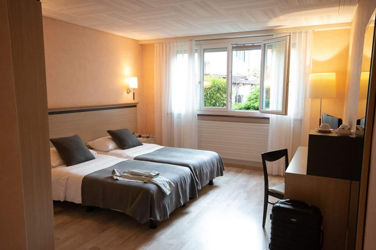A hotel room with two beds, a desk, a chair, and a window with curtains.