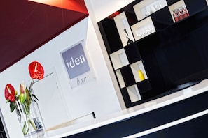 A modern interior with a white wall displaying the words "idea bar" and a glass vase with red flowers. - Idea Hotel Milano Malpensa Airport (Somma Lombardo)