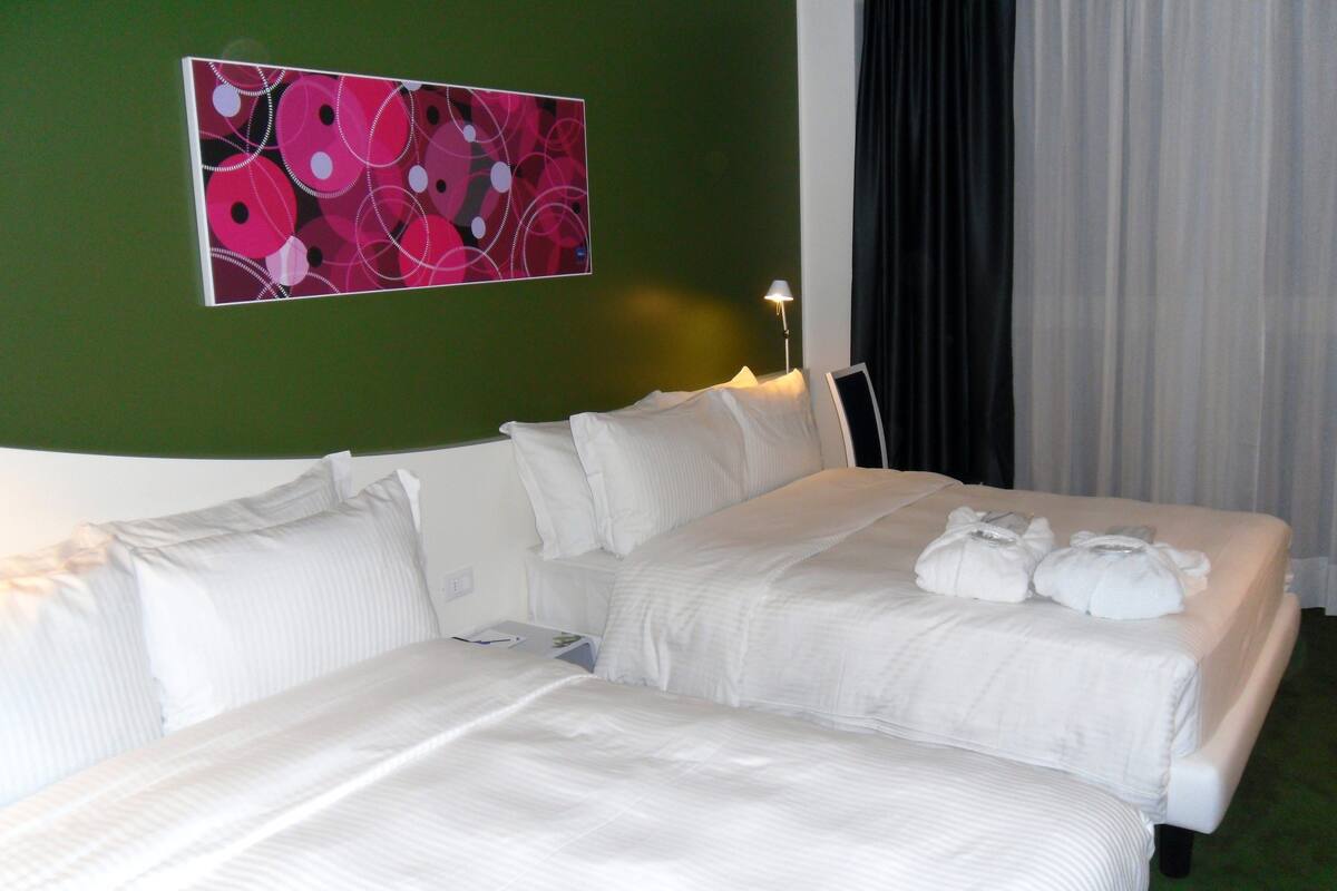 A hotel room with two beds, a green wall, and a painting.