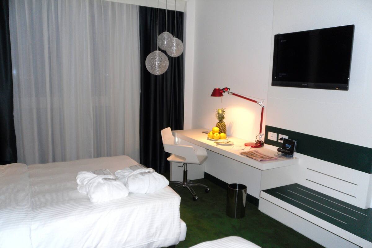 A hotel room with two beds, a desk, a chair, a TV, and a trash can.