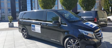 A black van parked in front of a building with a sign that reads "HOTEL MILANO MALPENSIA AIRPORT".