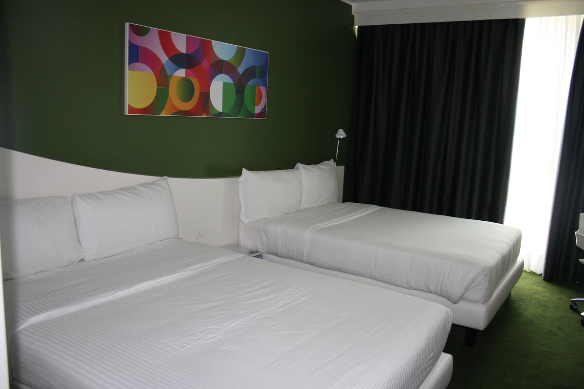 A hotel room with two beds, a green wall, and a colorful abstract painting.