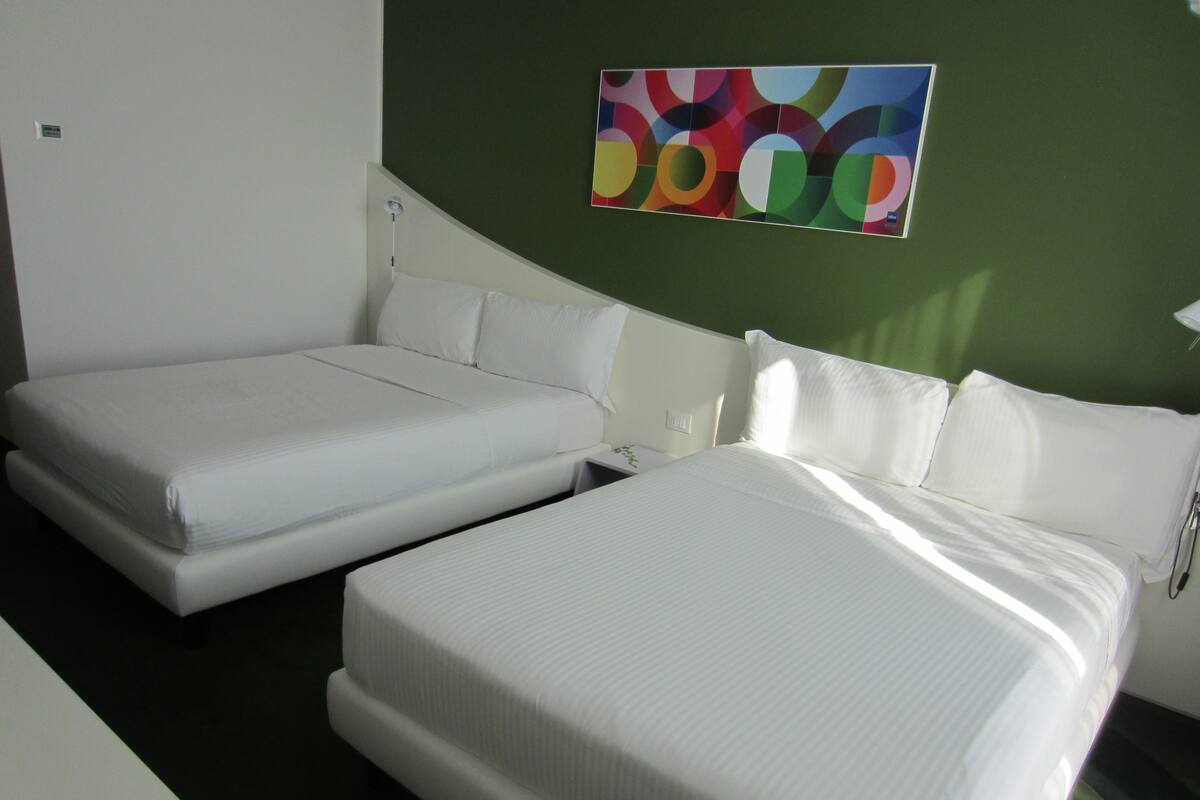 A hotel room with two single beds, a small bedside table, and a colorful abstract painting on the wall.