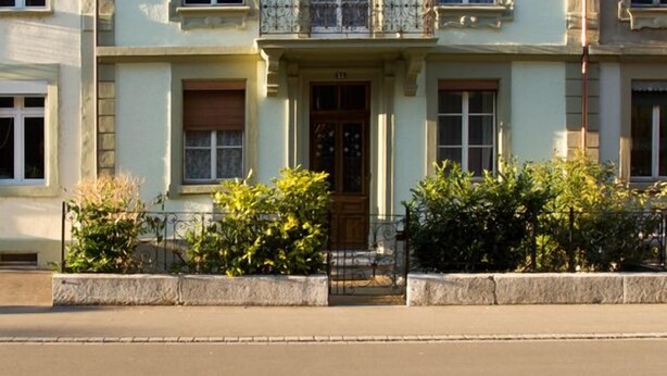 A multi-story building with a symmetrical facade, featuring evenly spaced windows, a central entrance with a door, and a small balcony on the second floor.